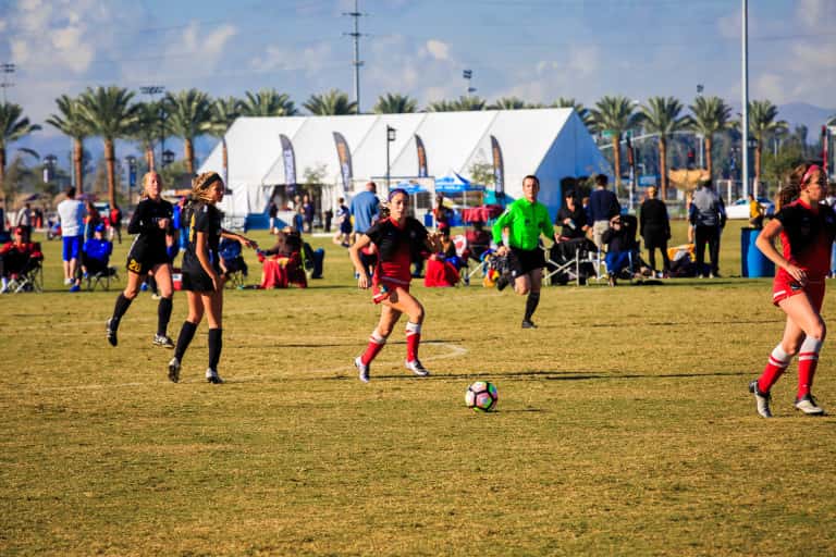 A girl running with the soccer ball down the field