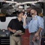 Two technicians inspecting underneath Mercedes-Benz on lift