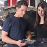 Mechanic showing the cost of service to female client while man working in background