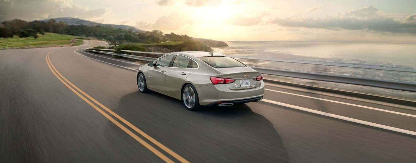 A tan 2024 Chevy Malibu from the rear at an angle after leaving a car dealer.