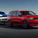 A red 2023 Dodge Durango towing a trailer to a used car dealership.