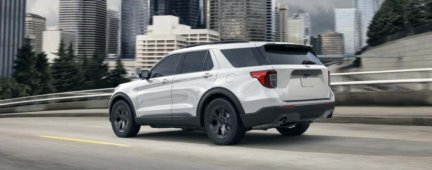 A white 2021 Ford Explorer driving down a hill near a city