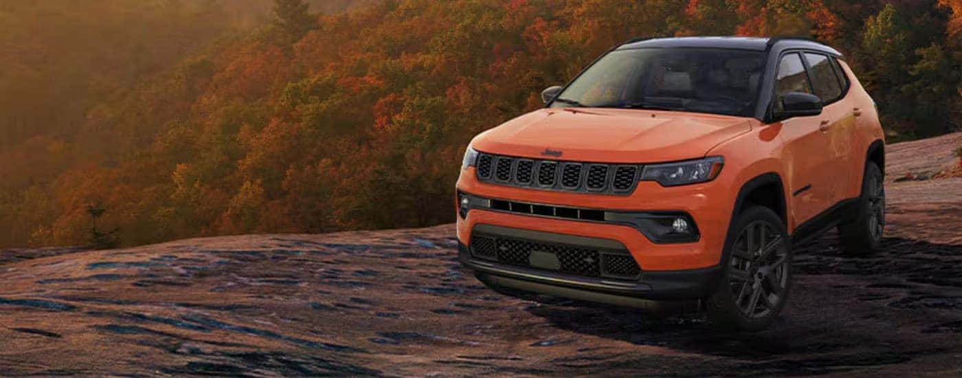 An orange 2025 Jeep Compass parked off-road overlooking a valley