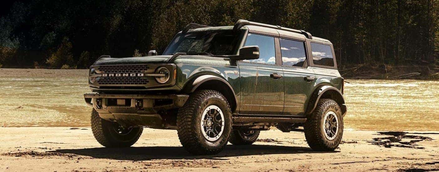 Green 2024 Ford Bronco Badlands parked off-road in front of a river