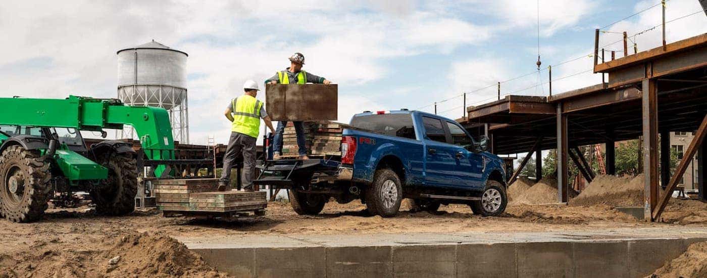 Construction workers loading pallets into the bed of a blue 2020 Ford F-250.