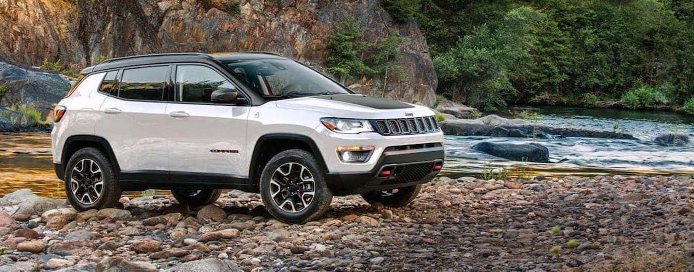 Side of a white 2020 Jeep Compass Trailhawk parked off-road near a lake.