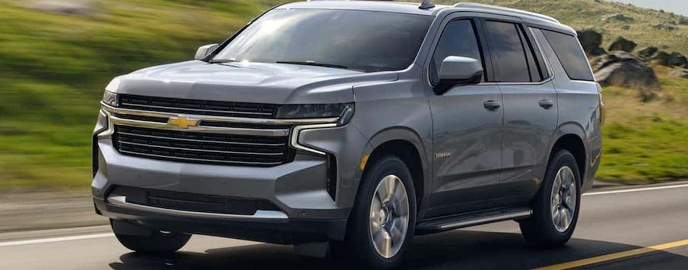 A silver 2021 Chevy Tahoe driving down a road in front of a sunny field