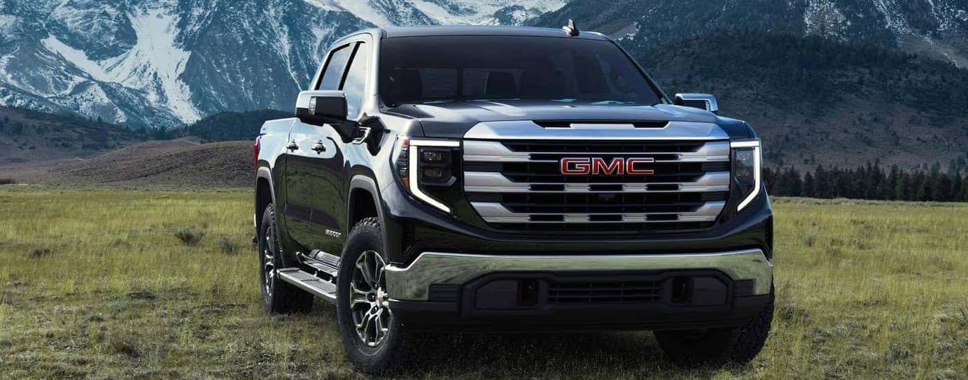 A black 2023 GMC Sierra 1500 parked in a field at the base of a mountain range
