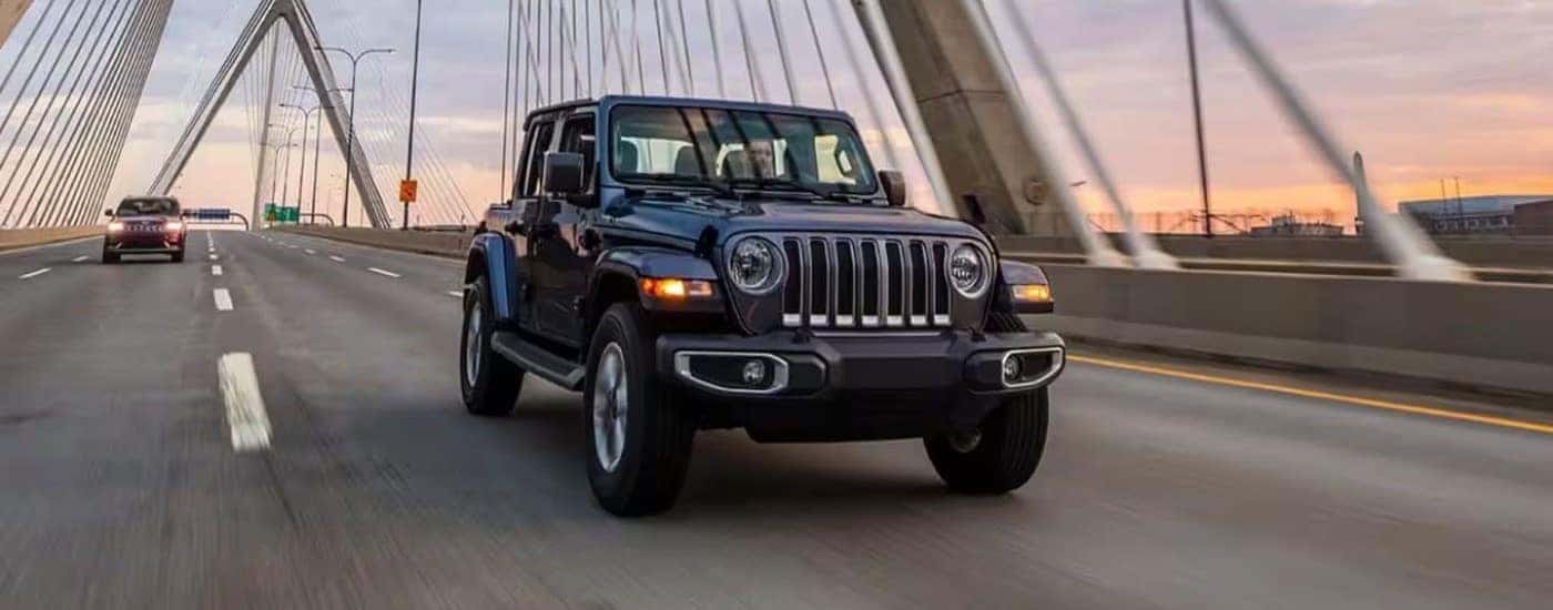A black 2023 Jeep Wrangler Unlimited driving over a bridge at sunset