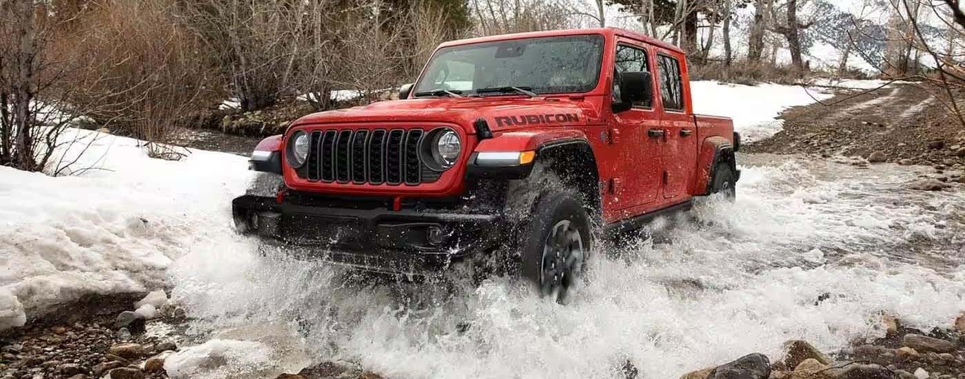 Red 2024 Jeep Gladiator driving through a stream