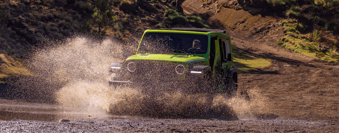A green 2026 Jeep Wrangler driving through muddy water off-road