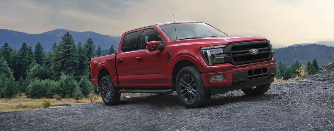 A red 2025 Ford F-150 Lariat parked off-road overlooking a forest valley