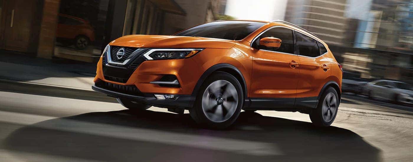 Orange 2020 Nissan Rogue Sport driving around a city street corner.