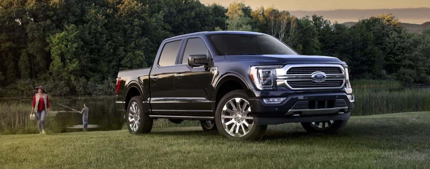 A black 2023 Ford F-150 parked by a pond and people fishing.