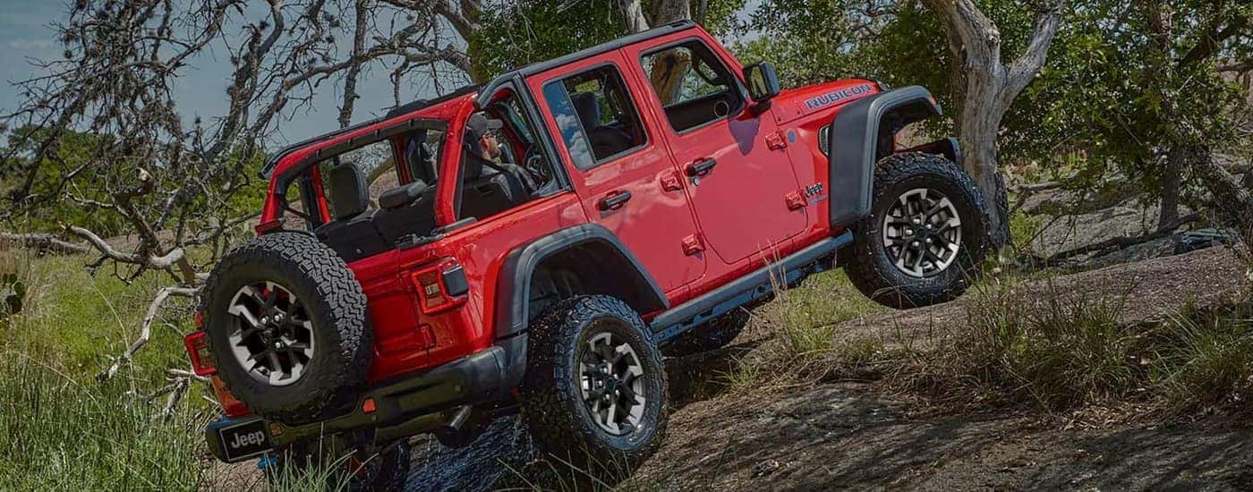 A red 2025 Jeep Wrangler Rubicon off-roading in water