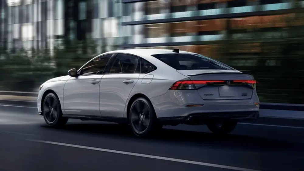 2026 Honda Accord Hybrid near Smithtown NY driving in the city, rear three quarter view highlighting fuel saving commuter performance