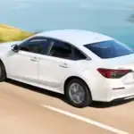 2026 Honda Civic Sedan near Smithtown NY driving along a coastal road, rear three quarter view showing smart value styling