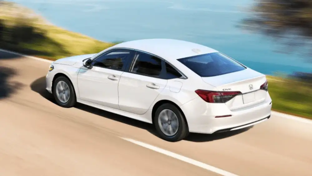 2026 Honda Civic Sedan near Smithtown NY driving along a coastal road, rear three quarter view showing smart value styling