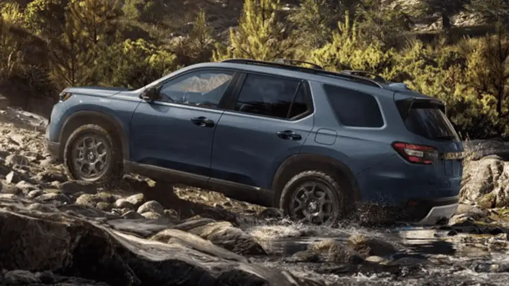 2025 Honda Pilot near Smithtown, NY driving off-road through rocky water crossing, showing SUV capability.