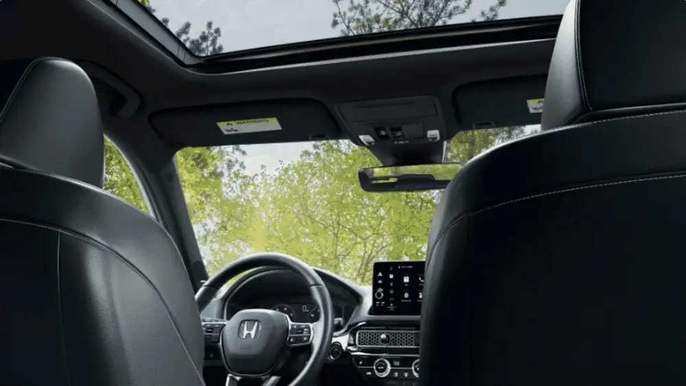 Honda Civic Hatchback near Smithtown, NY cabin view featuring front seats, dashboard layout, and panoramic sunroof.