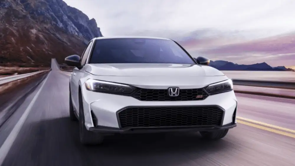 2026 Honda Civic Si near Smithtown, NY driving on an open highway, featuring a sporty front view and performance-focused styling.