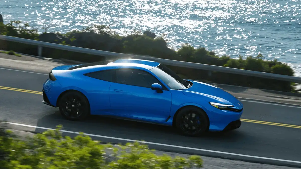 2026 Honda Prelude Hybrid near Smithtown, NY blue coupe driving along a coastal road, side view with ocean in the background