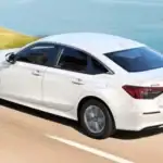 2026 Honda Civic Sedan Hybrid around Smithtown NY white sedan driving along a coastal road, rear three-quarter view for smooth commuting