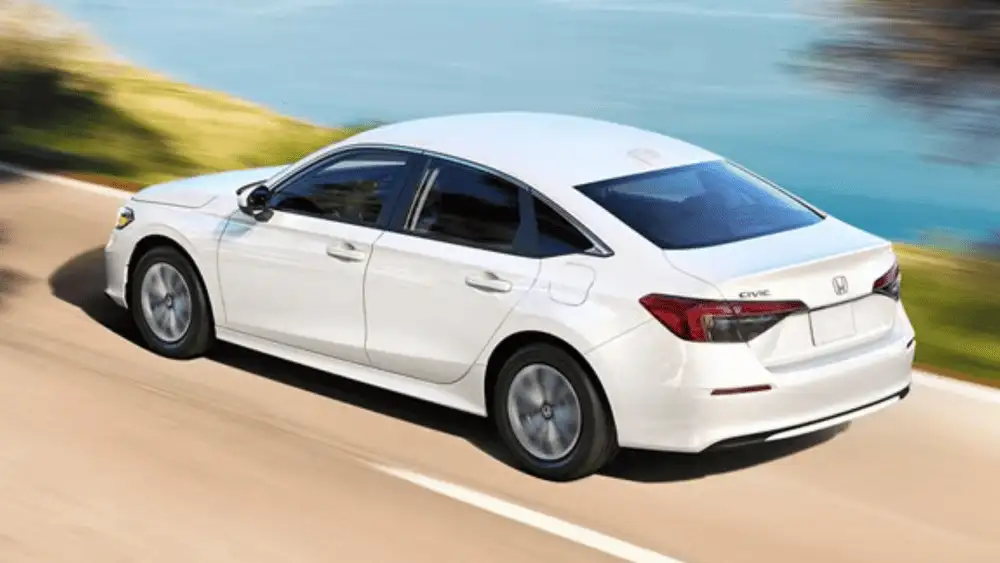 2026 Honda Civic Sedan Hybrid around Smithtown NY white sedan driving along a coastal road, rear three-quarter view for smooth commuting