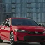 2026 Honda Civic Sedan in Rallye Red front three-quarter view in urban setting — smart April fuel savings for budget-conscious drivers near Commack NY