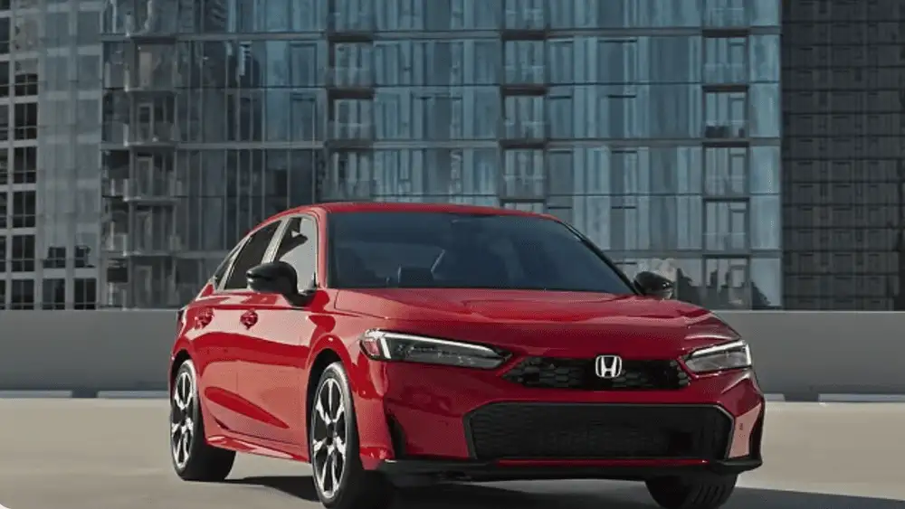 2026 Honda Civic Sedan in Rallye Red front three-quarter view in urban setting — smart April fuel savings for budget-conscious drivers near Commack NY