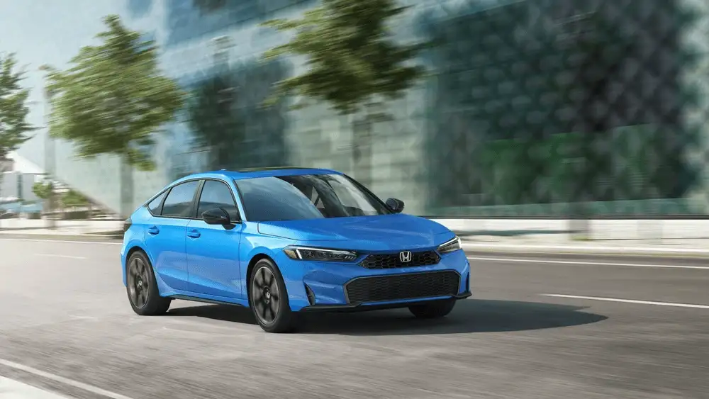 2026 Honda Civic Hatchback in Boost Blue Metallic front three-quarter view driving on city road near Commack NY