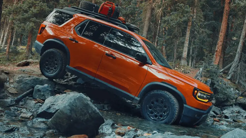 2026 Honda Passport TrailSport in Baja Orange climbing rocky terrain with roof rack in forest near Commack NY