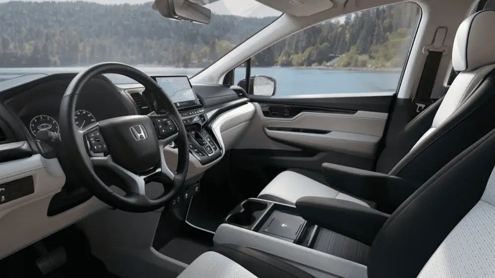 2026 Honda Odyssey minivan interior front cockpit with Honda steering wheel touchscreen and white trim near lake view