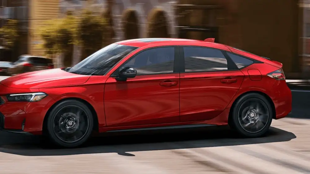 Red 2026 Honda Civic Hatchback Hybrid driving through town, showing off its cargo space advantages near Commack