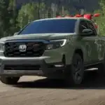 Olive green 2026 Honda Ridgeline hauling gear down a forest dirt road, a versatile truck choice near Hauppauge NY
