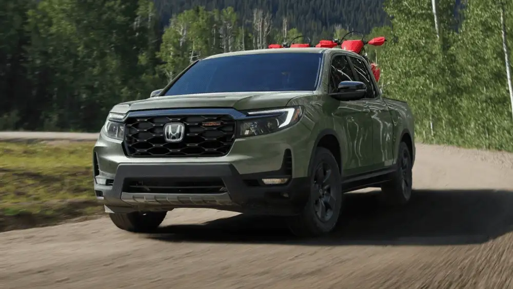 Olive green 2026 Honda Ridgeline hauling gear down a forest dirt road, a versatile truck choice near Hauppauge NY