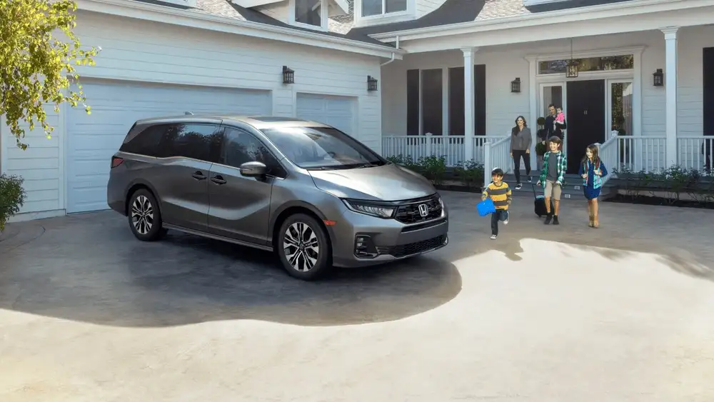 Gray 2026 Honda Odyssey near Hauppauge, NY, parked in a driveway with a family walking toward it.