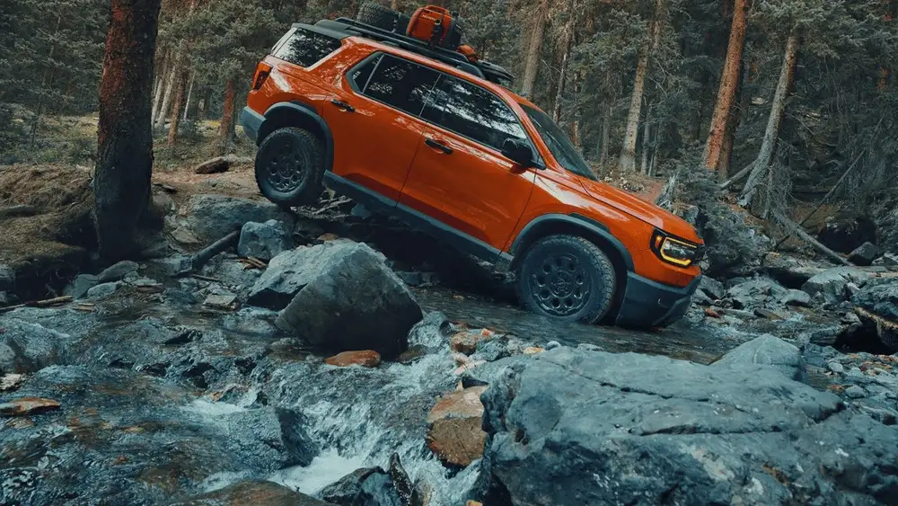 Orange 2026 Honda Passport near Hauppauge, NY, driving over rocks in a forest.