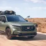 Green 2026 Honda CR-V near Hauppauge, NY, driving on a dirt road with a roof-mounted cargo carrier.