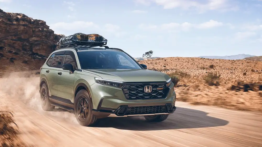 Green 2026 Honda CR-V near Hauppauge, NY, driving on a dirt road with a roof-mounted cargo carrier.