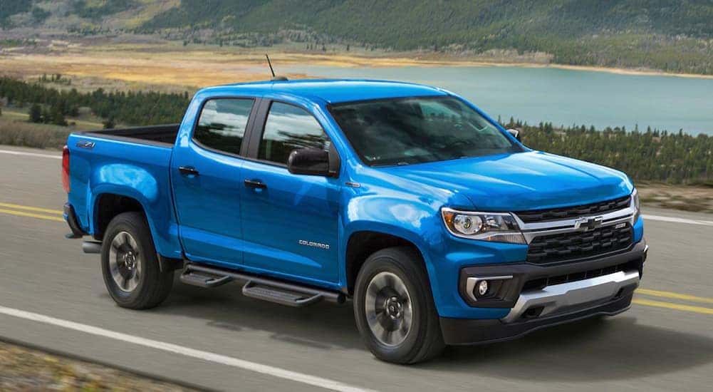 A blue 2021 Chevy Colorado is shown from the side driving down a road past a lake.