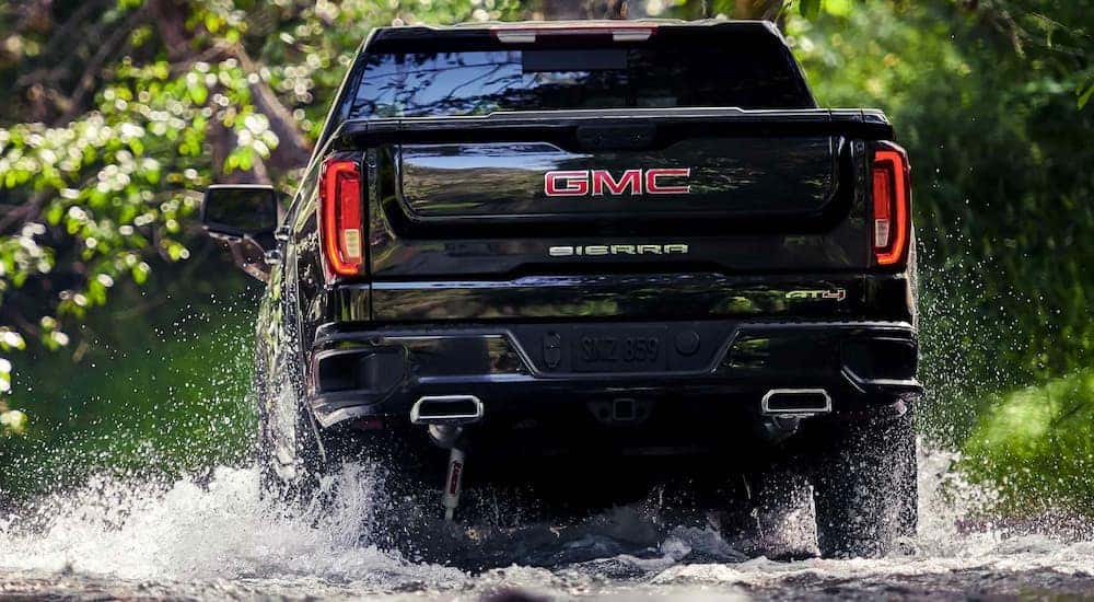 A black 2021 GMC Sierra 1500 AT4 is shown from behind driving through water after leaving a GMC dealer near you.