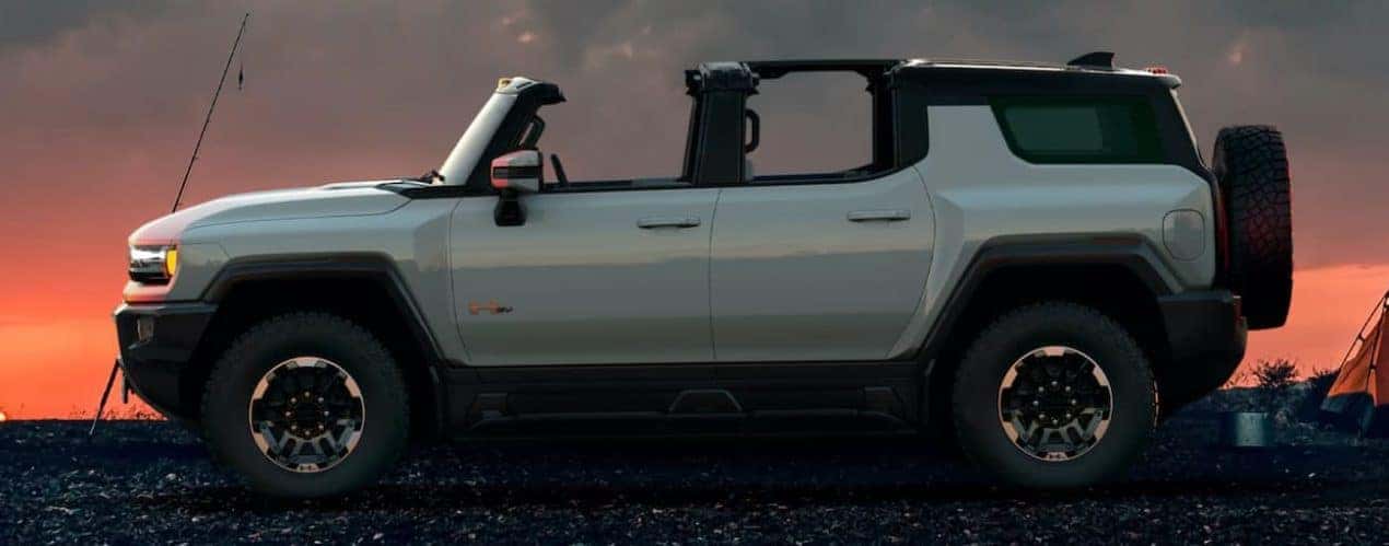 A white 2023 GMC Hummer EV SUV is shown from the side at sunset at a campsite.