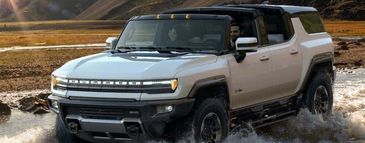 A white 2023 GMC Hummer EV SUV is off-roading in a river.