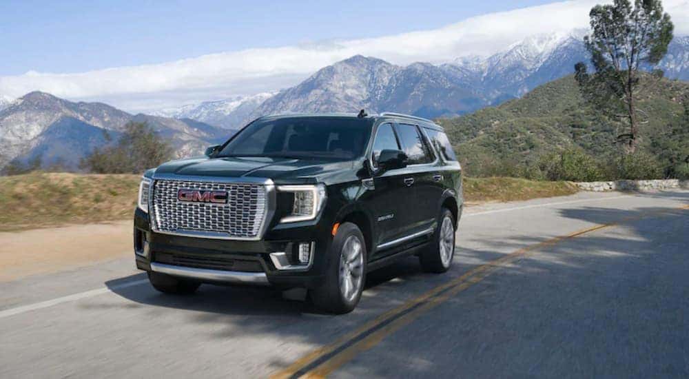 A black 2021 GMC Denali is shown driving on a two lane road in the mountains.