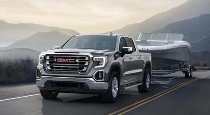 A silver 2021 GMC Sierra 1500 is towing a boat on a mountain road.