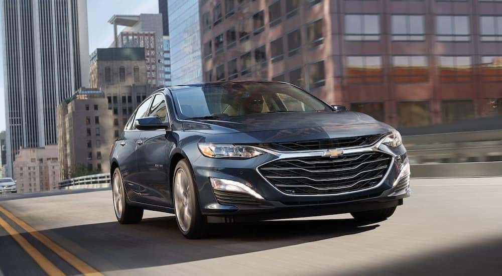 A blue 2020 Chevy Malibu is shown from the front driving through a city.
