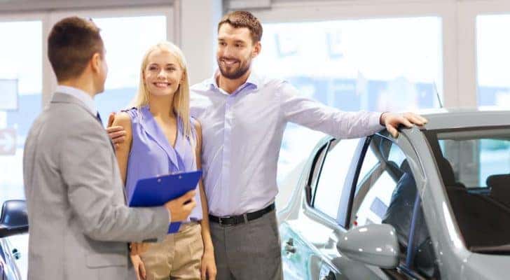 A couple is shown talking to a salesperson at a Shelbyville used car dealership.