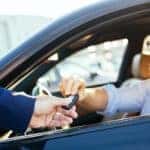 A person is sitting in the drivers seat of a car as a salesman passes them a set of keys at a Shelbyville used car dealership.