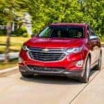 A red 2018 Chevy Equinox is shown driving through the suburbs after leaving a certified pre-owned Chevrolet dealer.